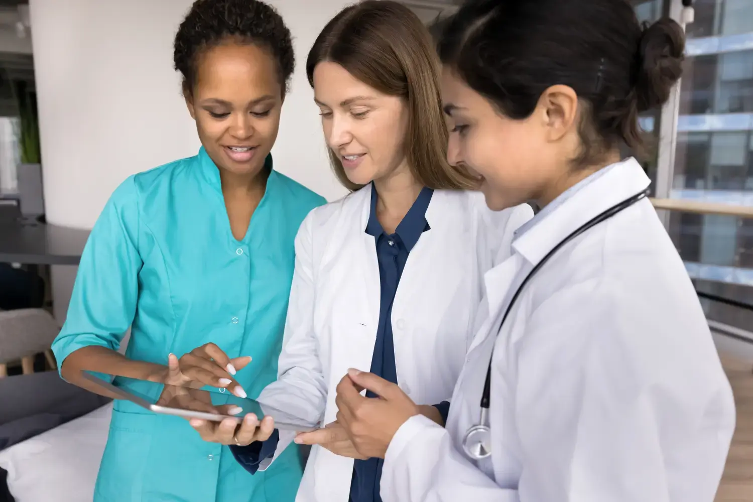 AMBULogic - Teamarbeit und Brainstorming. Medizinisches Team, drei multiethnische junge Frauen, studieren die elektronische Krankengeschichte des Patienten auf dem Tablet-PC-Bildschirm, besprechen die Diagnose und die Behandlung und verwenden KI, um die Daten zu analysieren und die Symptome zu überprüfen.